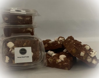 May include: Several pieces of Rocky Road Fudge in clear plastic containers and loose. The fudge is a dark brown color with white marshmallows and nuts. The label on the container reads "Pickens Rocky Road Fudge."