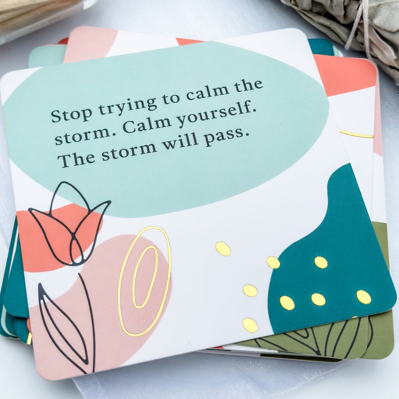 May include: A stack of inspirational cards with a white background. Each card features a pastel color palette with abstract floral and geometric designs. The text on the card reads: "Stop trying to calm the storm. Calm yourself. The storm will pass."