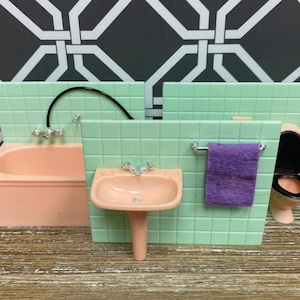 May include: A miniature bathroom set featuring a pink bathtub, sink, and toilet. The set includes a green tiled wall, a purple towel, and chrome fixtures. The background has a black and white geometric pattern.