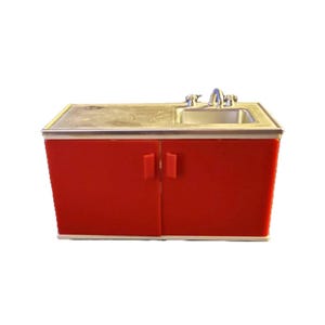 May include: A white ceramic mug with a black handle and the text "But First, Coffee" in a bold, black font. The mug is filled with a dark liquid, likely coffee, and sits on a light-colored surface.