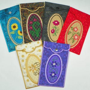 May include: Six different fabric pouches with embroidered floral designs. The pouches are in various colors, including blue, red, purple, gold, and black. Each pouch has a button closure and an oval-shaped embroidered design.