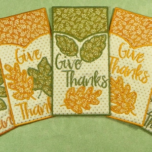 May include: Five embroidered fabric bookmarks with a fall theme. Each bookmark features a different design with leaves and the text "Give Thanks".