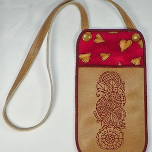 May include: A brown leather phone case with a red fabric flap featuring gold hearts. The case has a long brown leather strap and a detailed floral design on the front.