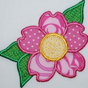 May include: A pink and green fabric flower with a yellow center. The flower has a polka dot pattern, a swirl pattern, and a striped pattern. The leaves are green with a textured pattern.