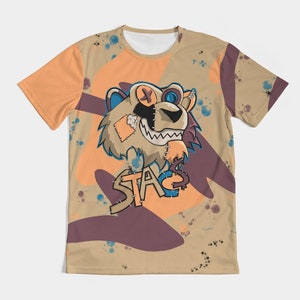 Op de afbeelding: Een beige T-shirt met een cartoon leeuwenontwerp. De leeuw heeft gestikte patches, een ooglapje en een knoog. Het woord "STA" staat eronder. Het T-shirt heeft een oranje en paars abstract ontwerp.