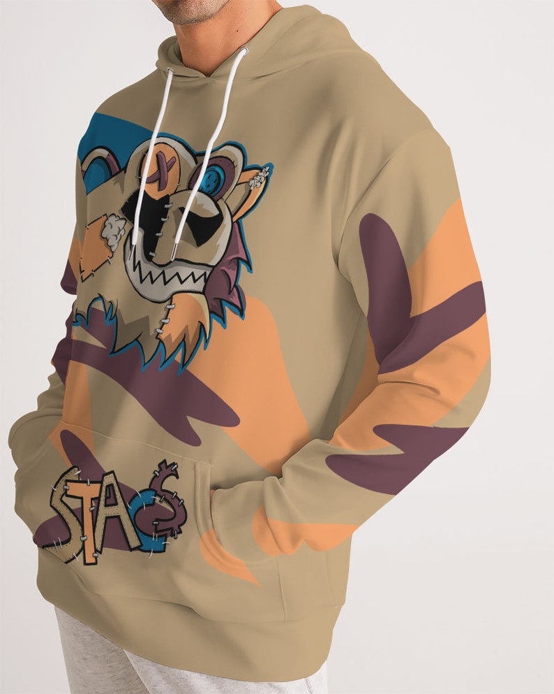 Puede incluir: Sudadera con capucha de color canela con un dise&ntilde;o de oso de dibujos animados. El oso tiene una cara cosida y una sonrisa. La sudadera con capucha tiene un bolsillo de canguro y la palabra "STA" cosida en el bolsillo. Formas abstractas naranjas y moradas decoran las mangas.
