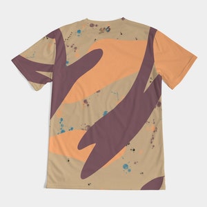 Op de afbeelding: T-shirt met korte mouwen met een beige achtergrond en abstracte vormen in oranje en donkerpaars. Het shirt heeft een ronde hals en een klein logo bij de halslijn. Blauwe en bruine verfspatten zijn over het shirt verspreid.