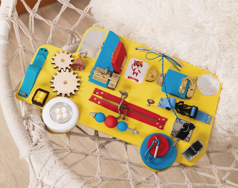 Busy board in the shape of track/bus with wheels and doors. The base is made of plywood. The thickness of the plywood is 10 mm (0.4 inches). Bright colors: yellow base, red and blue elements.