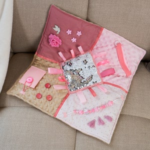 On the front part of the mat there are different fidget elements: Colorful Tassel pendants, felt decorations, Different textures of ribbons and fabrics