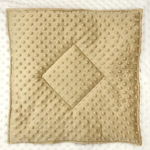May include: A square, tan-colored baby blanket with a textured, dimpled surface. The blanket features a quilted diamond pattern in the center. The edges are neatly finished, and the blanket appears soft and plush.