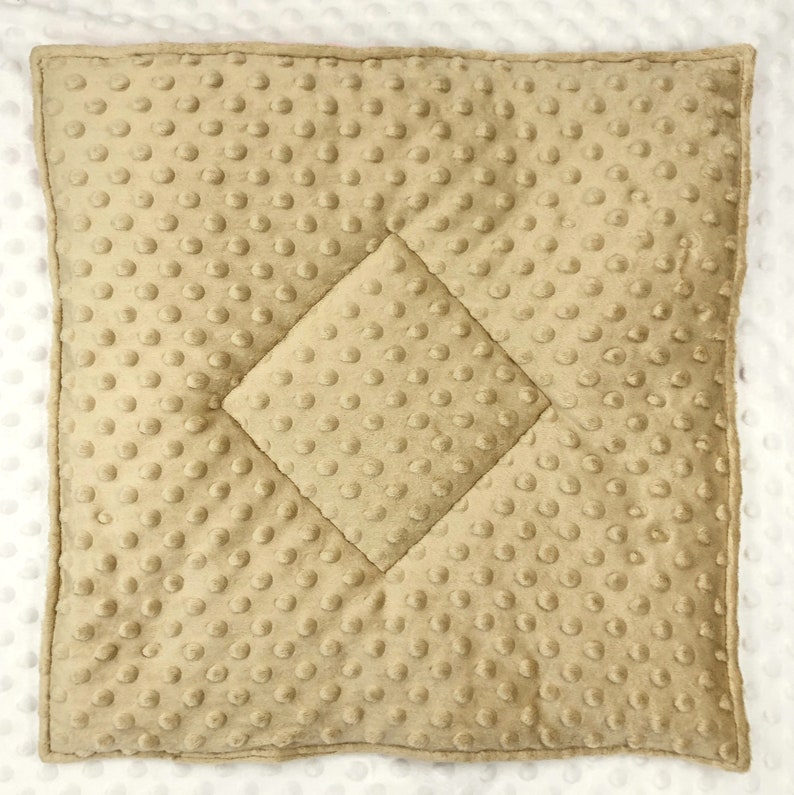 May include: A square, tan-colored baby blanket with a textured, dimpled surface. The blanket features a quilted diamond pattern in the center. The edges are neatly finished, and the blanket appears soft and plush.