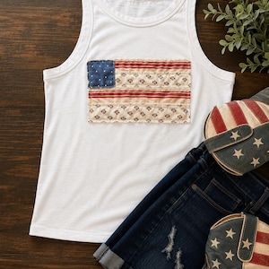 May include: White tank top with a patchwork American flag design. The flag features a blue square with white dots and red and cream stripes. Paired with denim shorts and star-spangled cowboy boots, this ensemble is perfect for a patriotic look.