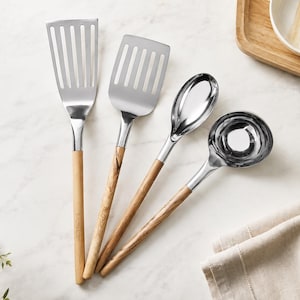 May include: A set of four kitchen utensils featuring polished stainless steel heads and light brown wooden handles. The set includes a long slotted turner, a wide slotted spatula, a solid serving spoon, and a deep round soup ladle.