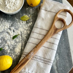 Pu&ograve; includere: Un cucchiaio di legno con un design unico del manico &egrave; appoggiato su un canovaccio a righe bianche e grigie. Sono presenti anche una ciotola di farina, due limoni e un tagliere di marmo. La parola "SALT YORK" &egrave; incisa sul cucchiaio.