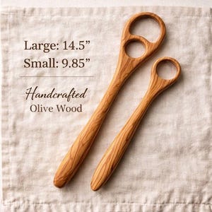 May include: Two handcrafted olive wood spoons. The larger spoon is 14.5 inches long, and the smaller spoon is 9.85 inches long. The spoons have a natural wood grain pattern and a circular handle opening.