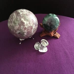 May include: Three crystal spheres on a purple surface. One sphere is green and white, one is purple and white, and one is clear.