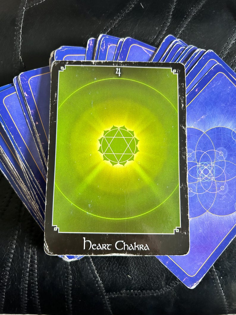 May include: A green and black tarot card with the number 4 and the words "Heart Chakra" printed on it. The card features a green circle with a yellow star in the centre.