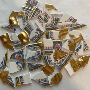 May include: Scattered fragments of a broken porcelain dish. The pieces feature gold trim, floral patterns in pink and blue, and white backgrounds. Some fragments have a solid gold finish.