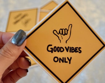 May include: Yellow diamond-shaped sticker with a black border. The sticker has a black hand making the shaka sign and the text "Good Vibes Only".