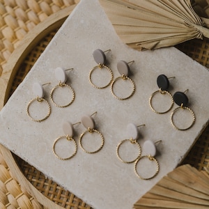 May include: A set of six pairs of earrings with gold hoops and round clay charms in beige, gray, and black.