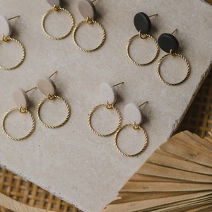 May include: A set of six pairs of earrings with gold hoops and round clay charms in beige, black, and white.