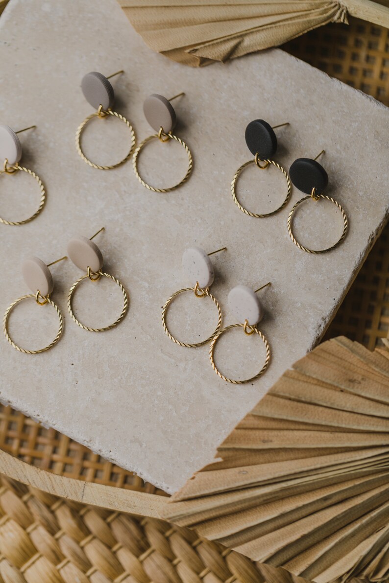 May include: A set of six pairs of earrings with gold hoops and round clay charms in beige, black, and white.