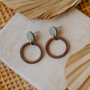 May include: A pair of wooden hoop earrings with a green circle accent. The earrings are on a white surface.