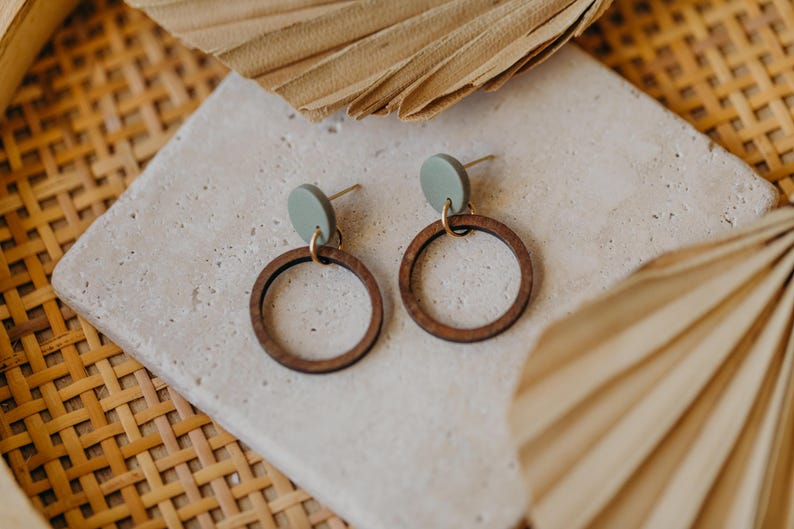 May include: A pair of wooden hoop earrings with a green circle accent. The earrings are on a white surface.