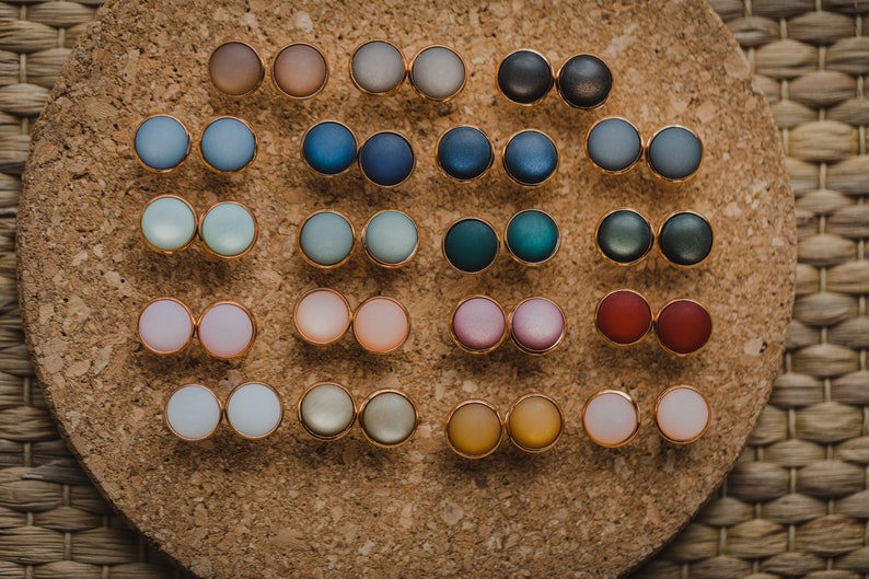 Pu&ograve; includere: Un set di 20 paia di orecchini rotondi in resina colorata. Gli orecchini sono esposti su un pannello di sughero.