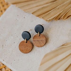 May include: A pair of earrings with black and brown round wooden discs. The earrings have gold posts.