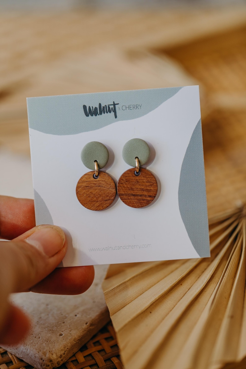May include: A pair of earrings with a green clay top and a brown wood bottom. The earrings are on a white card with the text "Walnut & Cherry" and a website address.