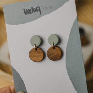 May include: A pair of earrings featuring a light green and brown wood design. The earrings are displayed on a white card with the text "Walnut x Cherry" and "www.walnutandcherry.com".