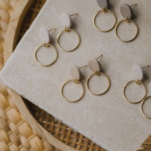 May include: A set of six pairs of earrings with gold hoops and beige and light brown circular ceramic accents.