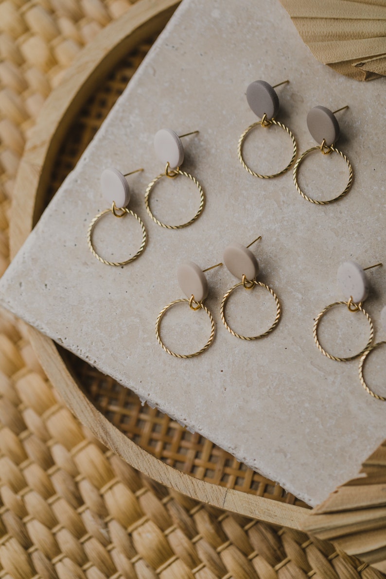 May include: A set of six pairs of earrings with gold hoops and beige and light brown circular ceramic accents.