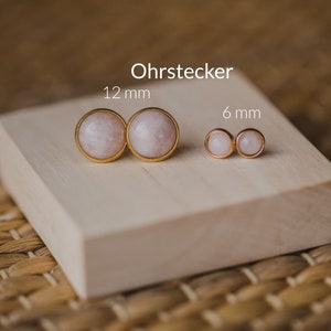 May include: Two pairs of gold stud earrings with round white stones. The larger pair measures 12 mm and the smaller pair measures 6 mm.