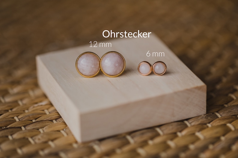 May include: Two pairs of gold stud earrings with round white stones. The larger pair measures 12 mm and the smaller pair measures 6 mm.