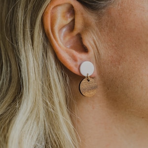May include: A pair of dangle earrings with a white ceramic top and a brown wood bottom.