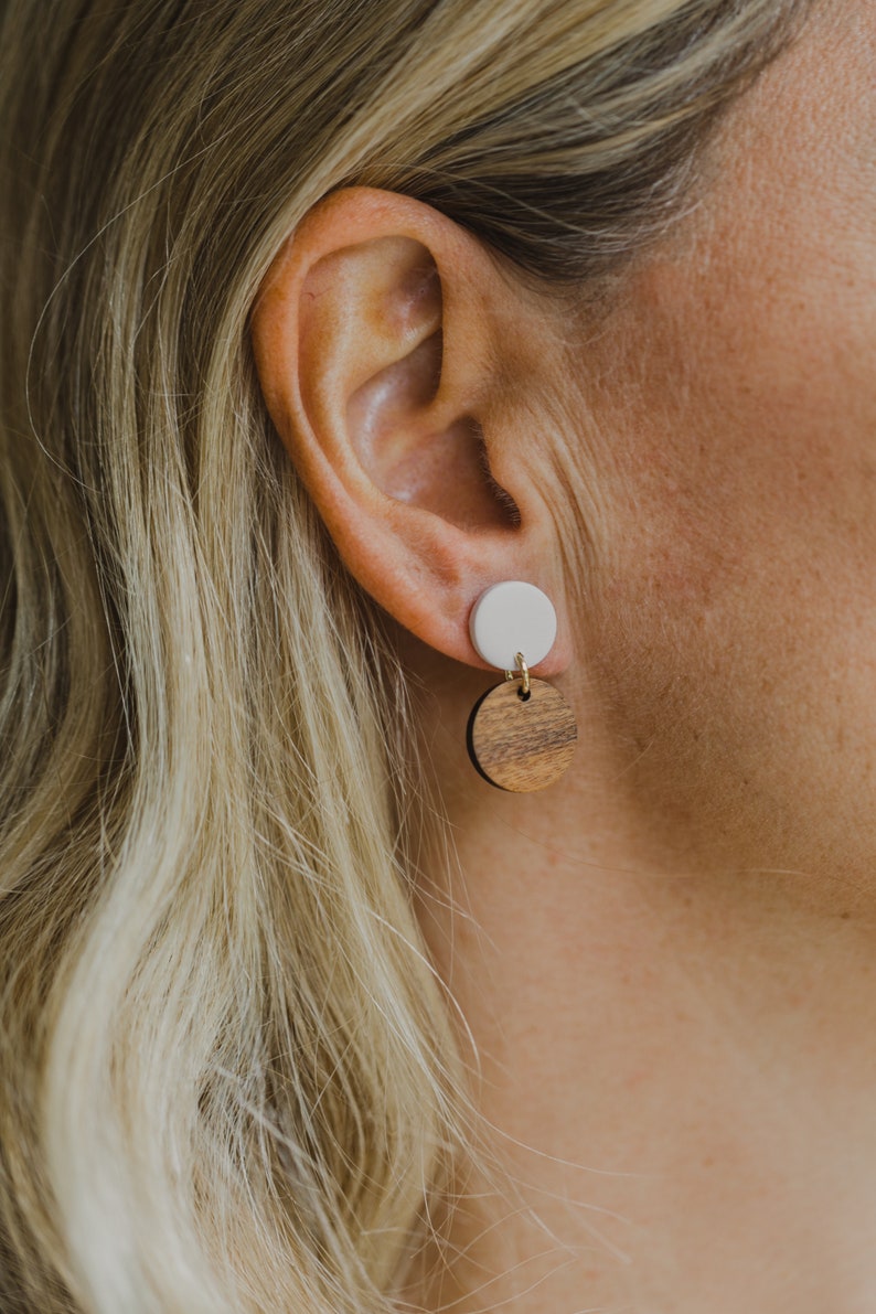 May include: A pair of dangle earrings with a white ceramic top and a brown wood bottom.
