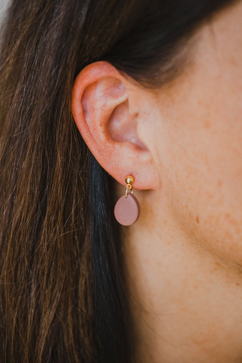 May include: A pair of brown clay earrings with gold posts. The earrings are shaped like small circles.