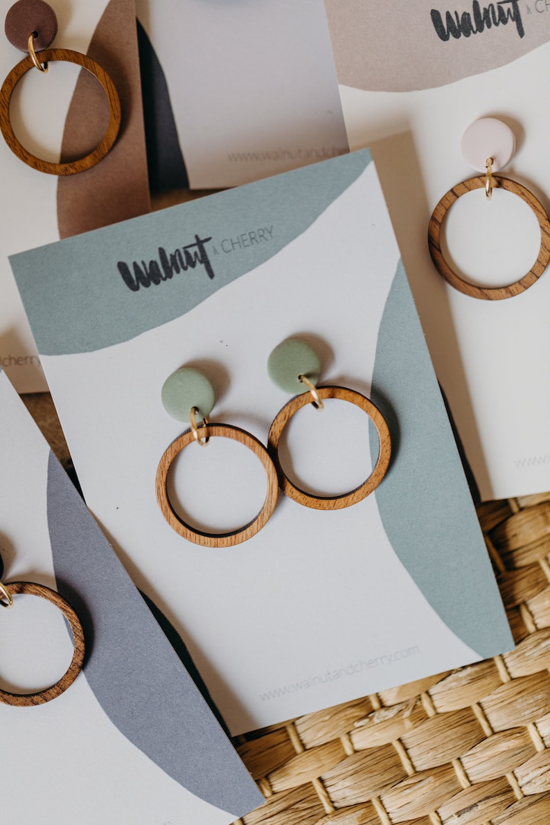 May include: A pair of wooden earrings with green clay accents. The earrings are on a white card with the text "Walnut + Cherry" and a website address.