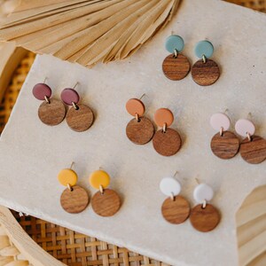 Puede incluir: Surtido de pendientes de madera y arcilla en varios colores, incluyendo turquesa, marr&oacute;n, naranja, amarillo, rosa y blanco. Los pendientes se muestran en una superficie blanca.