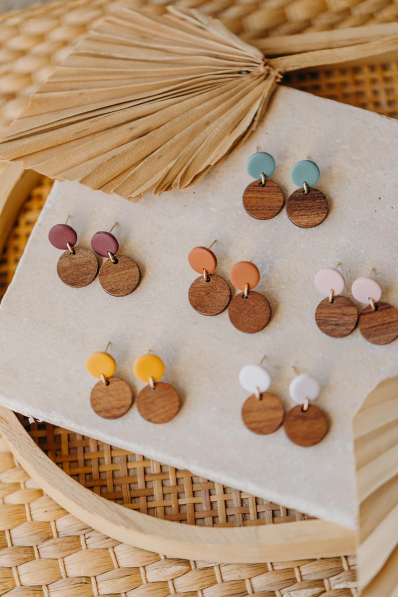 Puede incluir: Surtido de pendientes de madera y arcilla en varios colores, incluyendo turquesa, marr&oacute;n, naranja, amarillo, rosa y blanco. Los pendientes se muestran en una superficie blanca.