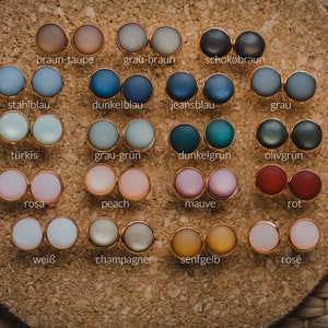 Pu&ograve; includere: Un set di 16 paia di orecchini rotondi in vetro colorato con montature dorate. Gli orecchini sono disposti in quattro file di quattro paia ciascuna. I colori includono marrone, grigio, blu, verde, rosa, pesca, malva, rosso, bianco, champagne, giallo e rosa.