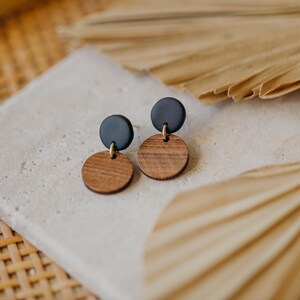 May include: A pair of earrings with black and brown wooden circles. The earrings are on a white surface with a brown woven background.