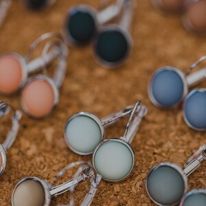 May include: Assortment of colorful round earrings with silver hoops. The earrings feature a variety of colors, including blue, green, pink, and brown.