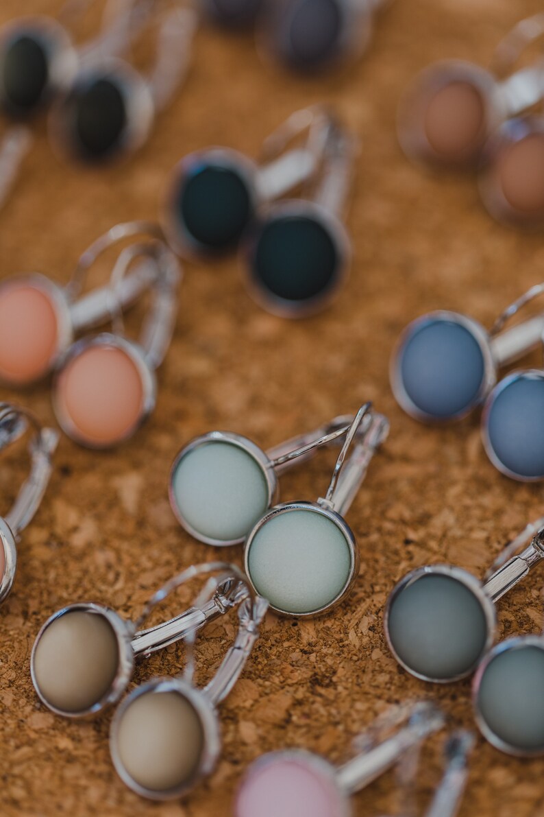 May include: Assortment of colorful round earrings with silver hoops. The earrings feature a variety of colors, including blue, green, pink, and brown.