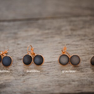 May include: Four pairs of earrings with different colored glass cabochons. The earrings are in shades of blue and brown. The colors are labeled "dunkelblau", "jeansblau", "grau-blau", and "schokobraun".