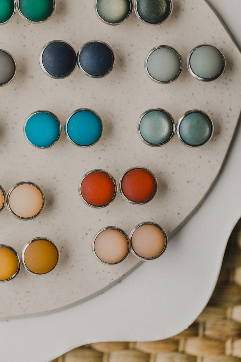 Op de afbeelding: Een assortiment van kleurrijke ronde oorbellen die op een wit oppervlak worden gepresenteerd. De oorbellen zijn gemaakt van verschillende materialen, waaronder metaal, glas en plastic. De oorbellen zijn in paren gerangschikt, waarbij elk paar een andere kleur heeft.