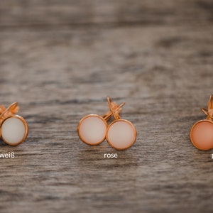 May include: Three pairs of earrings with different colored stones. The earrings are gold-toned and have a simple design. The stones are creme-white, rose, and peach.
