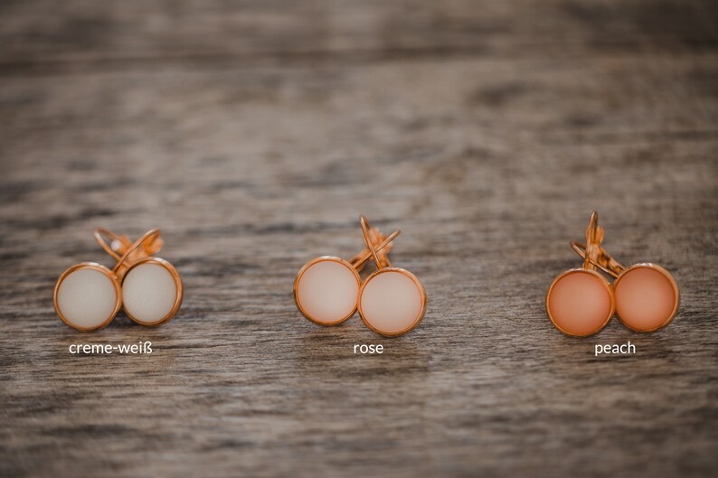 May include: Three pairs of earrings with different colored stones. The earrings are gold-toned and have a simple design. The stones are creme-white, rose, and peach.